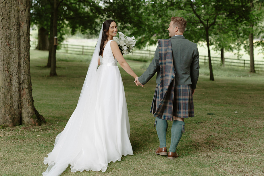 Bride and groom walking away holding hands with bride looking back to camera